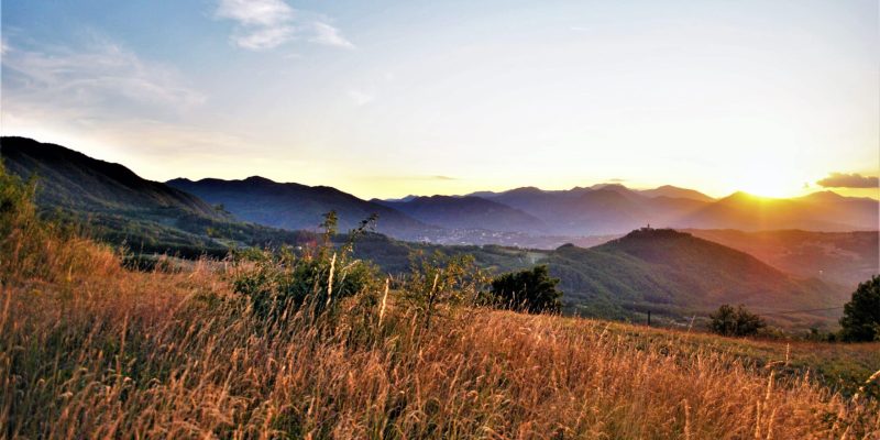 Tramonto su un paesaggio montano con campi dorati in primo piano.